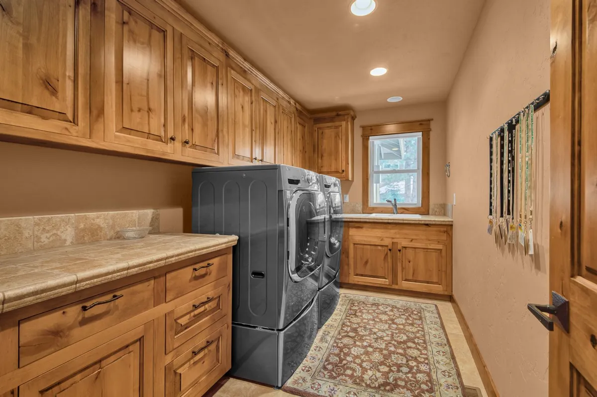 A functional laundry room equipped with a washer and dryer, wooden cabinetry for storage, and a cozy rug for homey comfort. The space is tidy and welcoming, perfect for managing family needs during a stay.