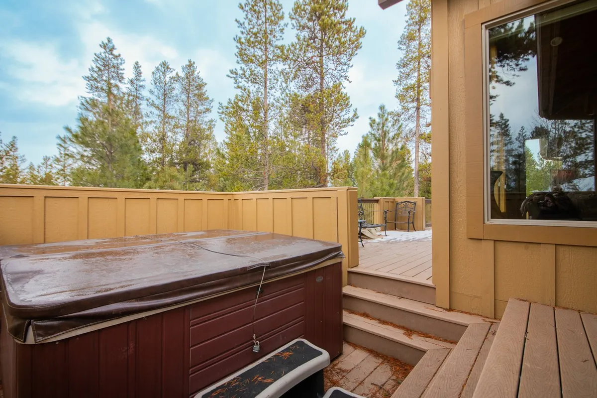 An inviting private deck bordered by trees, featuring a bubbling hot tub and outdoor seating for relaxation. The view and natural setting create an ideal spot for socializing, enjoying mountain air, or a peaceful soak after a day of adventure.