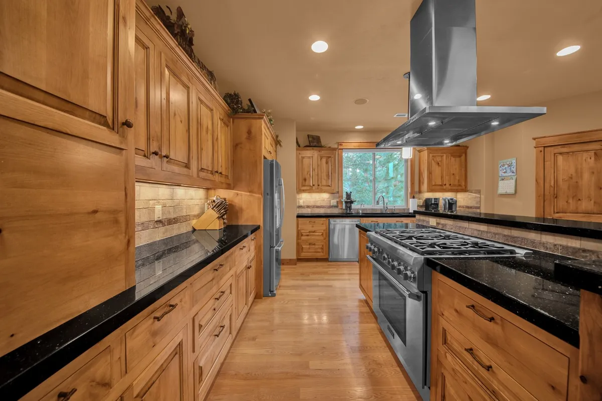 A modern, well-equipped kitchen featuring granite countertops, stainless steel appliances, warm wood cabinetry, and a large window letting in natural light. The kitchen layout includes generous prep space and an inviting atmosphere for group meal prep and casual gatherings.