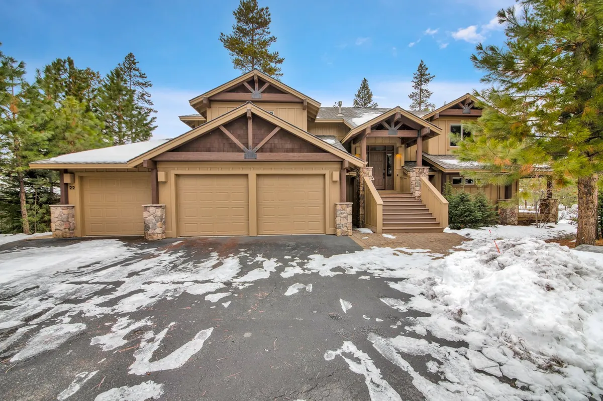 This image displays the home's exterior with a clear view of the garage doors, a snow-covered driveway, and the surrounding trees, emphasizing accessible and protected parking options. The scene captures the house in a cozy winter setting, highlighting the year-round practicality of the garage and driveway for vehicles and gear.
