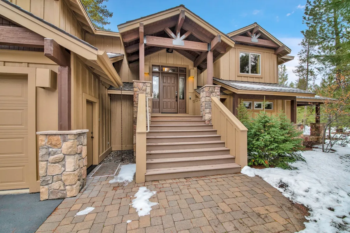 The image features the inviting front entrance of the home, with stone details, wooden beams, and a staircase leading to the door. While the garage isn't the primary focus, the image provides context for how guests and residents access the home and the welcoming ambiance of the property.