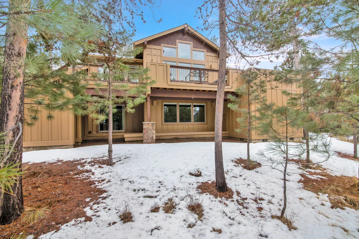 The exterior of a wooden home with large windows, nestled among pine trees and blanketed by snow. The scene evokes a cozy, inviting atmosphere ideal for winter retreats and group get-togethers.