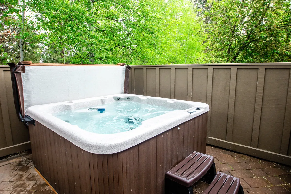 An inviting outdoor hot tub on a deck surrounded by lush greenery. The area exudes tranquility, offering a secluded spot for relaxation under the sky—ideal for moonlit soaks or peaceful mornings.