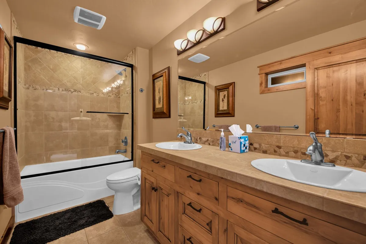 A sparkling hall bath with a double sink vanity, glass shower enclosure, and a mirrored wall. The space feels bright, modern, and highly functional, ideal for accommodating multiple guests.