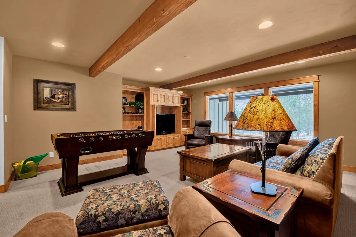 A lively lower-level entertainment space featuring a foosball table, wooden furniture, large windows for natural light, and a comfortable atmosphere for socializing, playing games, or relaxing together.