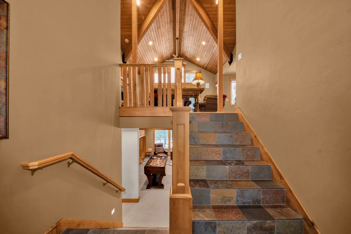 A view of the home's entrance area, showing a staircase with wooden railings, high ceiling, and a comfortable furniture arrangement. The design is both welcoming and practical, ideal for coming and going throughout the seasons.