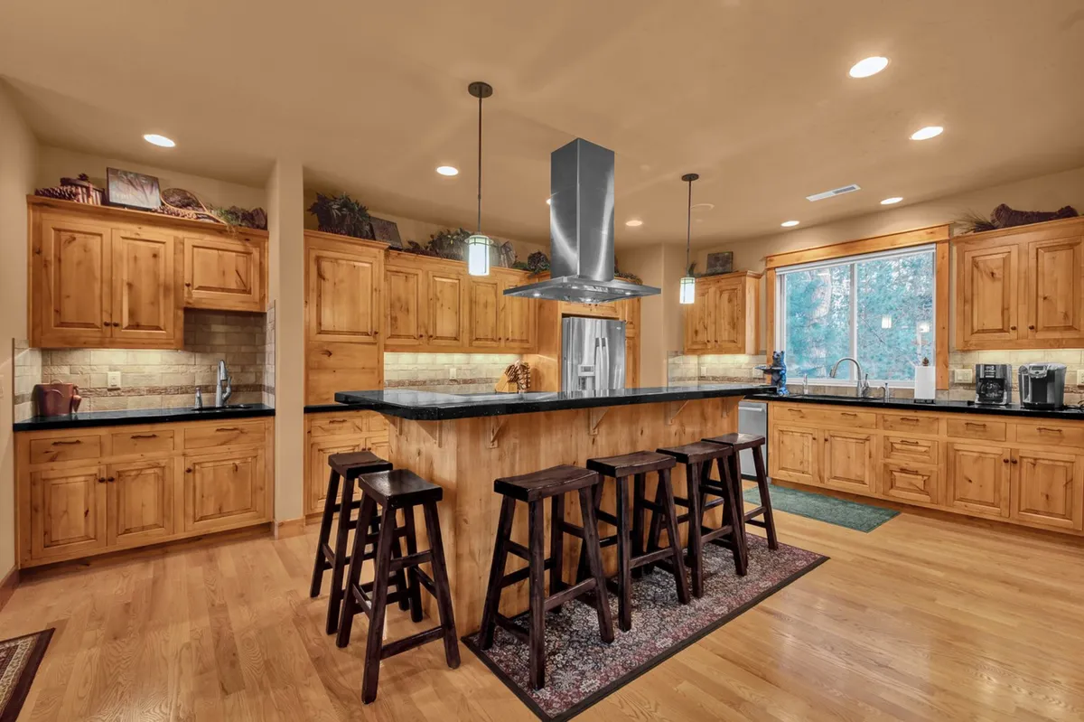 A spacious, sunlit kitchen with a large island, stools, wooden cabinetry, and a window letting in natural light. The setting is perfect for cooking, entertaining, or casual family gatherings, contributing to the feeling of an upscale yet welcoming retreat.