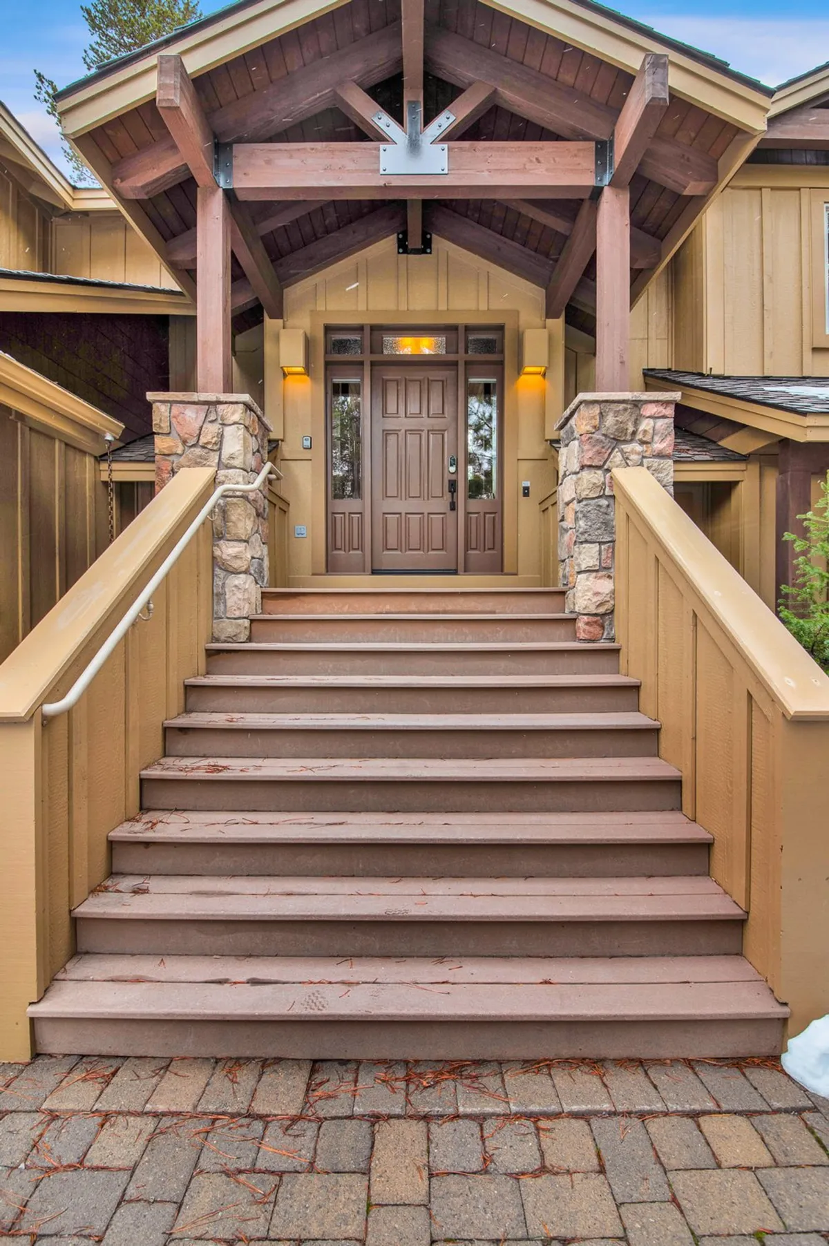 An up-close view of the home's entrance with wooden steps, stone pillars, and an overhead canopy. The inviting porch area sets the stage for welcoming guests, with ample room for kids to play or families to gather before heading out on adventures.
